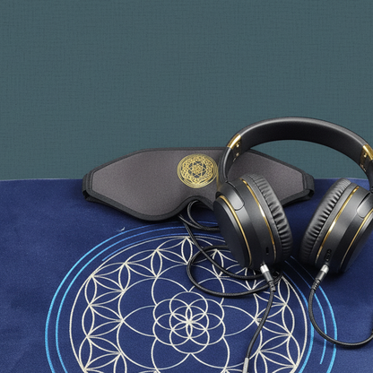 A close-up view of a vibroacoustic therapy zafu meditation cushion bundle showing a lavender cushion with a gold lotus mandala, over-ear headphones, and a satin eye mask arranged against a muted teal studio background. — for Carpe Diem Dream