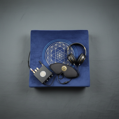 A vibroacoustic therapy zafu meditation cushion bundle featuring a blue cushion with a gold lotus mandala, a compact black amplifier, over-ear headphones, and a satin eye mask arranged on a soft gray studio background. — for Carpe Diem Dream