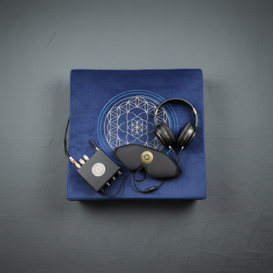 A vibroacoustic therapy zafu meditation cushion bundle featuring a blue cushion with a gold lotus mandala, a compact black amplifier, over-ear headphones, and a satin eye mask arranged on a soft gray studio background. — for Carpe Diem Dream