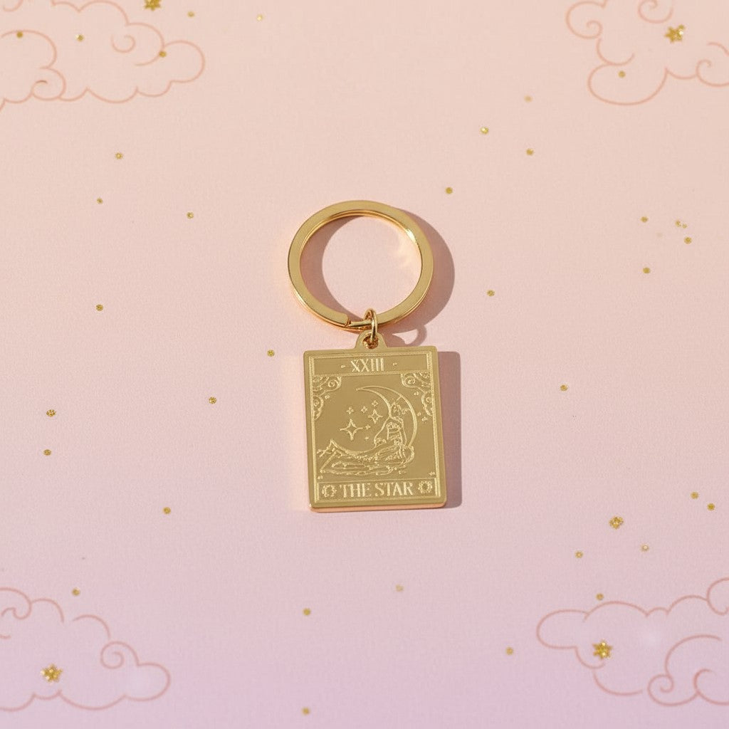 The Star keyring from the Vintage Tarot Card Keyring collection, featuring an engraved gold star and celestial design on a soft pastel pink background with subtle clouds, styled for Carpe Diem Dream.