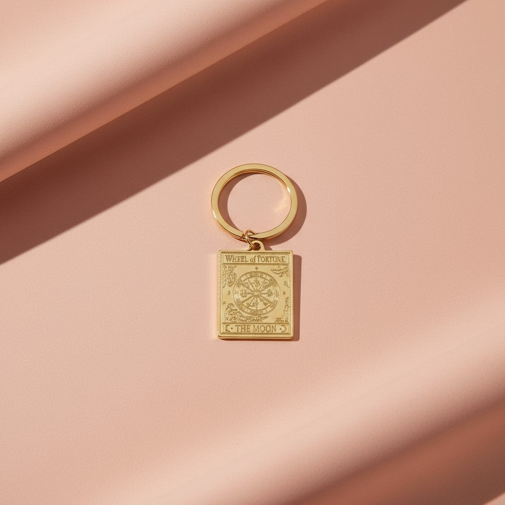 The Wheel of Fortune keyring from the Vintage Tarot Card Keyring collection, featuring an engraved gold wheel design on a soft blush-toned background, styled for Carpe Diem Dream.