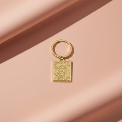 The Wheel of Fortune keyring from the Vintage Tarot Card Keyring collection, featuring an engraved gold wheel design on a soft blush-toned background, styled for Carpe Diem Dream.