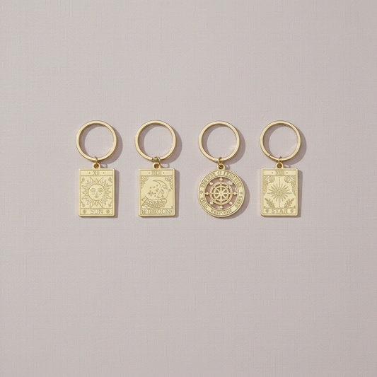 Set of four vintage-style gold tarot keyrings displayed on a soft neutral background, each engraved with symbolic sun, moon, wheel, and star designs – for Carpe Diem Dream.