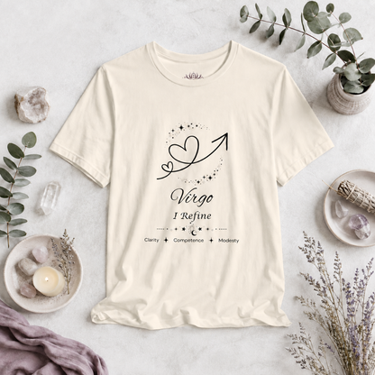 Virgo Rising I Refine zodiac T-shirt in Natural with black celestial heart and arrow artwork and Clarity, Competence, Modesty text, styled in a cool-toned studio botanical flat lay. — for Carpe Diem Dream