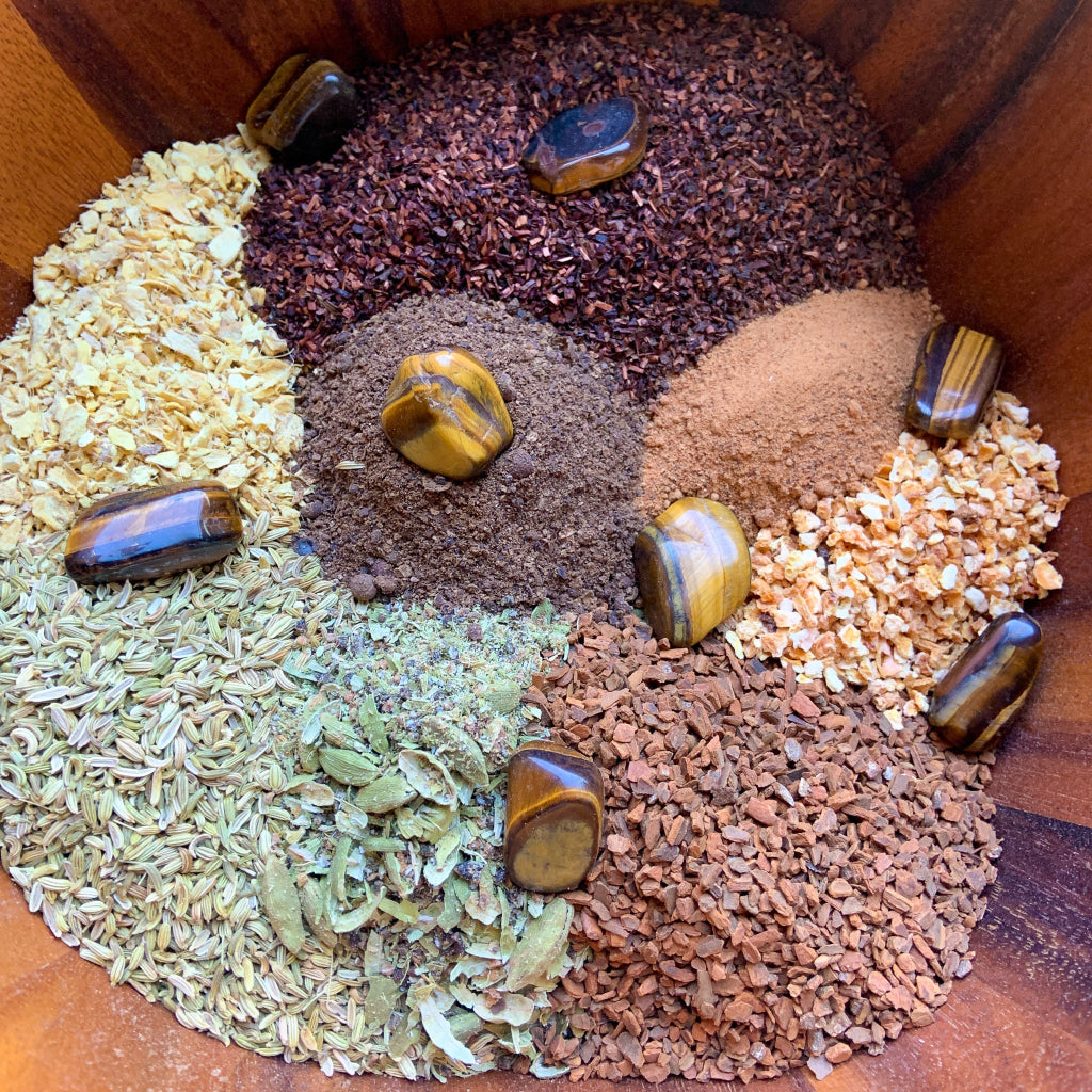 Supplier ingredient display showing the individual organic herbs and spices used in Vitality Chai Tea arranged in a wooden bowl with polished Tiger's Eye crystals, highlighting the handcrafted crystal-infused blend — for Carpe Diem Dream