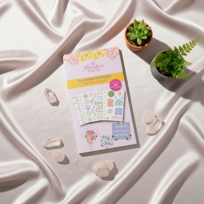 Wellness Edit planner sticker book displayed on white draped fabric with crystals and small succulents in soft natural light — for Carpe Diem Dream