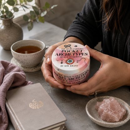 The Wild Unknown Pocket Archetypes Deck & Guidebook by Kim Krans held naturally in both hands during a quiet moment of self-reflection with tea, soft textures, and rose quartz in a cool-toned Carpe Diem Dream sanctuary setting. — for Carpe Diem Dream