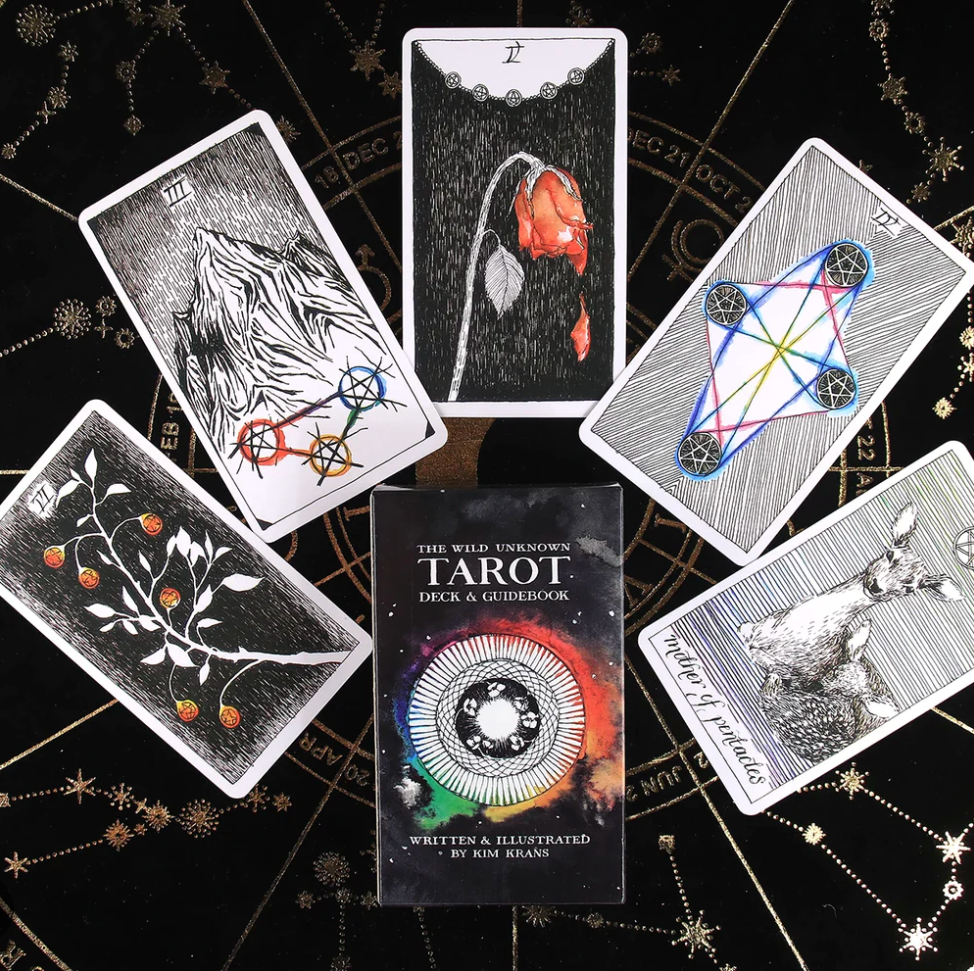 A spread of illustrated tarot cards from The Wild Unknown Tarot deck arranged around the deck box on a dark symbolic background, showing the artwork and card style. — for Carpe Diem Dream