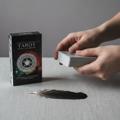 Hands holding and drawing from a stack of Wild Unknown Tarot cards beside the deck box on a linen surface, showing real use and scale. — for Carpe Diem Dream