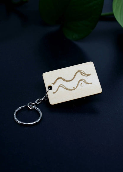 Wood Engraved Zodiac Keychain featuring Aquarius astrology symbol, handcrafted from natural wood blue background with green plant for Carpe Diem Dream