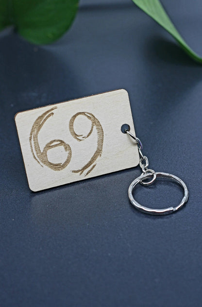 Wood Engraved Zodiac Keychain featuring Cancer astrology symbol, handcrafted from natural wood blue background with green plant for Carpe Diem Dream