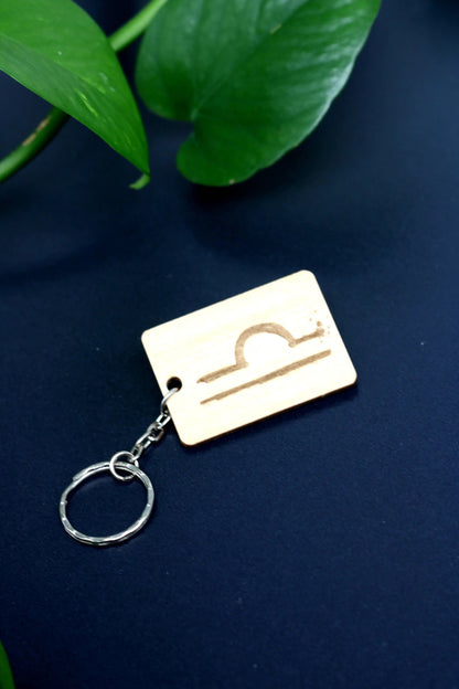 Wood Engraved Zodiac Keychain featuring Libra astrology symbol, handcrafted from natural wood blue background with green plant for Carpe Diem Dream