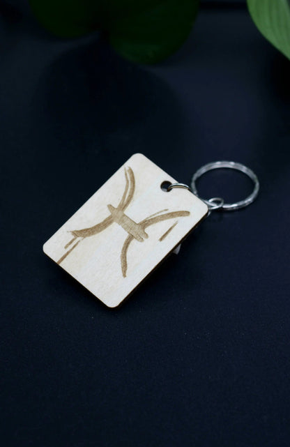 Wood Engraved Zodiac Keychain featuring Pisces astrology symbol, handcrafted from natural wood blue background with green plant for Carpe Diem Dream