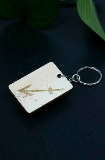 Wood Engraved Zodiac Keychain featuring Sagittarius astrology symbol, handcrafted from natural wood blue background with green plant for Carpe Diem Dream