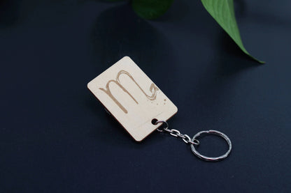 Wood Engraved Zodiac Keychain featuring Scorpio astrology symbol, handcrafted from natural wood blue background with green plant for Carpe Diem Dream