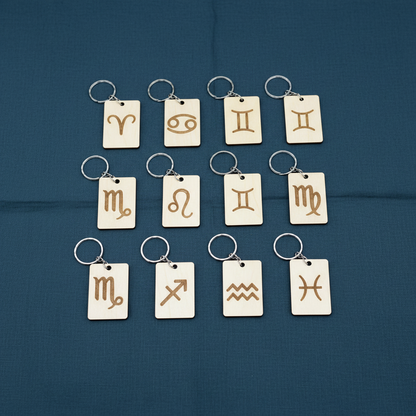 Wood Engraved Zodiac Keychains — All 12 , on textured linen dark teal background.
