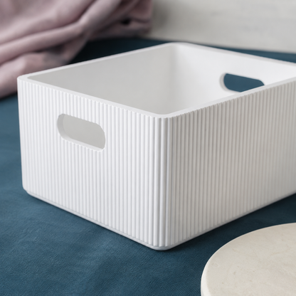 Close-up of a white wooden ribbed storage bin showing fluted texture, rounded corners, and smooth cutout handles with soft mauve linen accents. — for Carpe Diem Dream