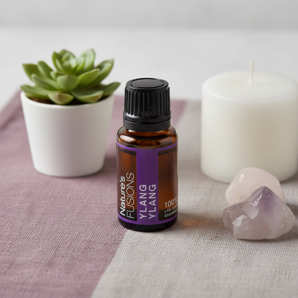 A 15ml amber glass bottle of Ylang Ylang essential oil with a black cap and purple label displayed on a soft linen surface beside rose quartz crystals, a white candle, and a small green plant. — for Carpe Diem Dream