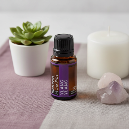 A 15ml amber glass bottle of Ylang Ylang essential oil with a black cap and purple label displayed on a soft linen surface beside rose quartz crystals, a white candle, and a small green plant. — for Carpe Diem Dream