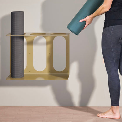 Gold metal yoga mat wall bracket holding a gray rolled yoga mat while a person places a green rolled yoga mat beside it. — for Carpe Diem Dream