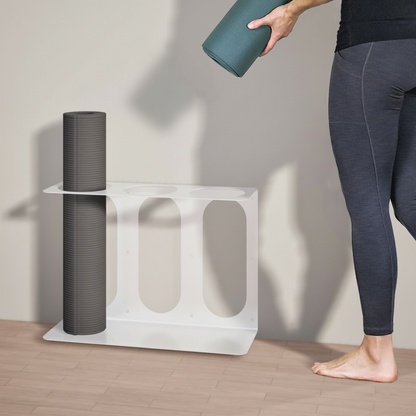 White metal yoga mat wall bracket holding a dark gray rolled yoga mat while a person places a green rolled yoga mat beside it. — for Carpe Diem Dream