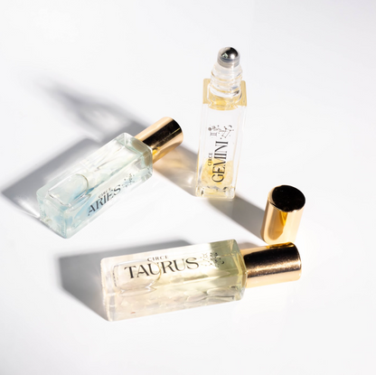 Close-up of zodiac gemstone perfume oil rollerball bottles labeled Aries, Gemini, and Taurus with gold caps on a bright white background. — for Carpe Diem Dream